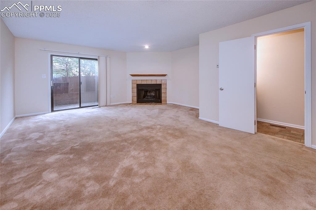 Image 15 of 24: Unfurnished living room featuring a tiled fireplace and light colored carpe