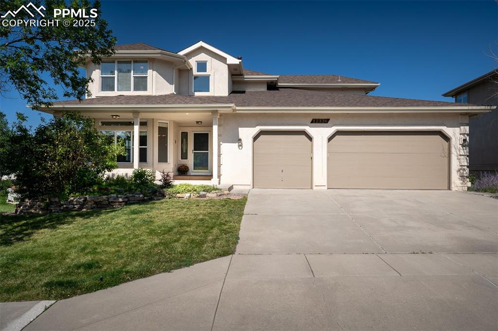 Caption: View of front facade with covered porch, roof with shingles, stucco siding, concrete driveway, and a