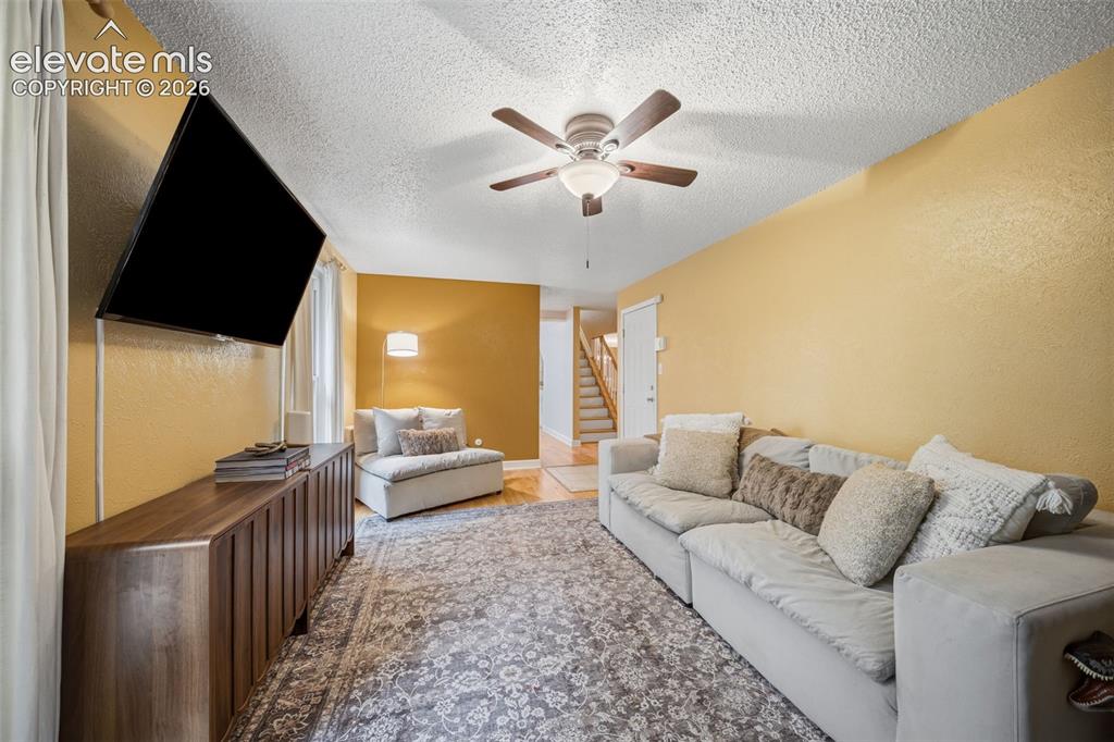 Image 10 of 42: Living area with textured walls, wood-finish flooring, and a ceiling fan wi