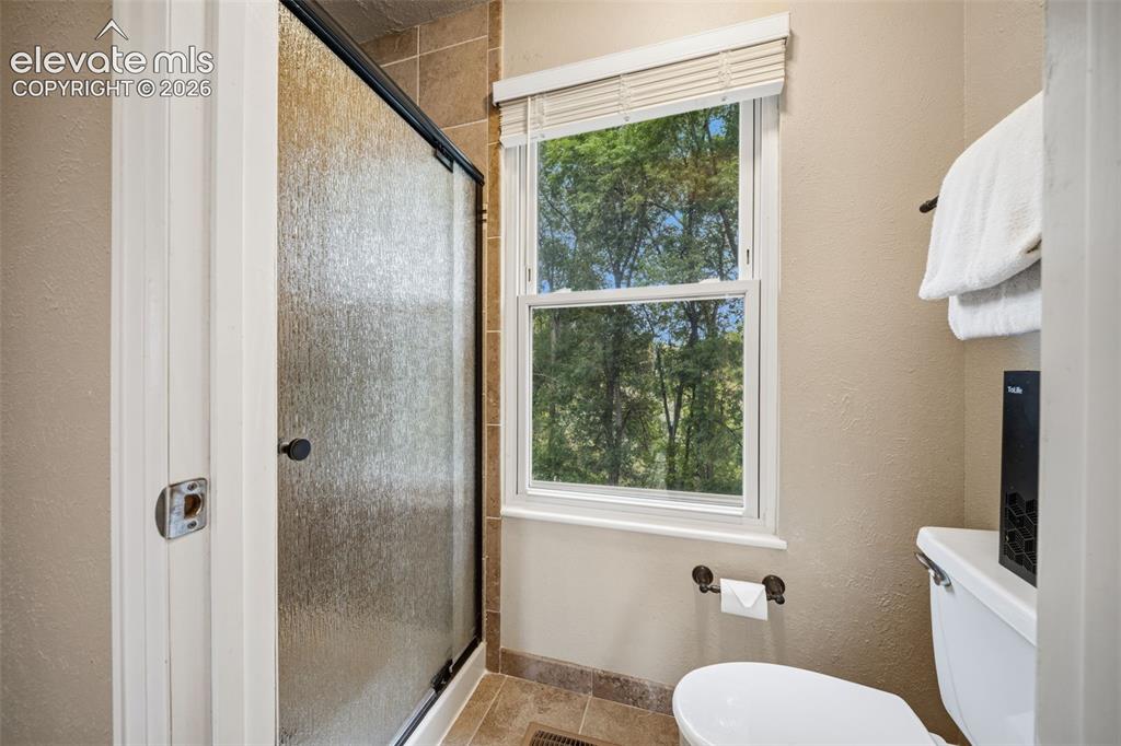 Image 22 of 42: Shower enclosure with textured glass doors, a single window, and tiled floo