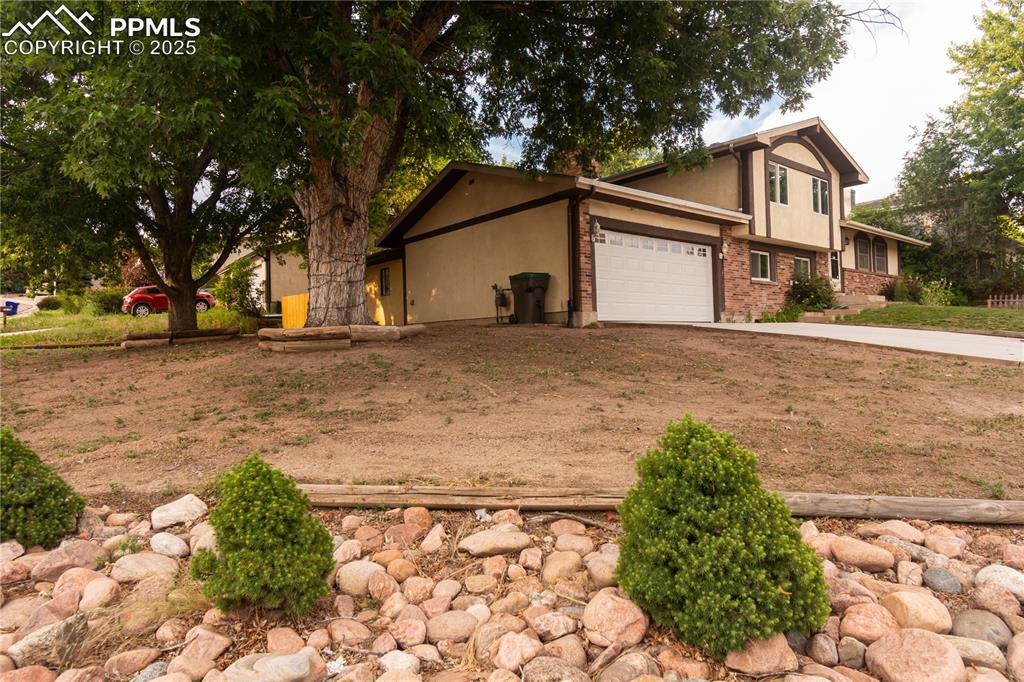 Caption: View of side of home with concrete driveway, stucco siding, brick siding, and an attached garage