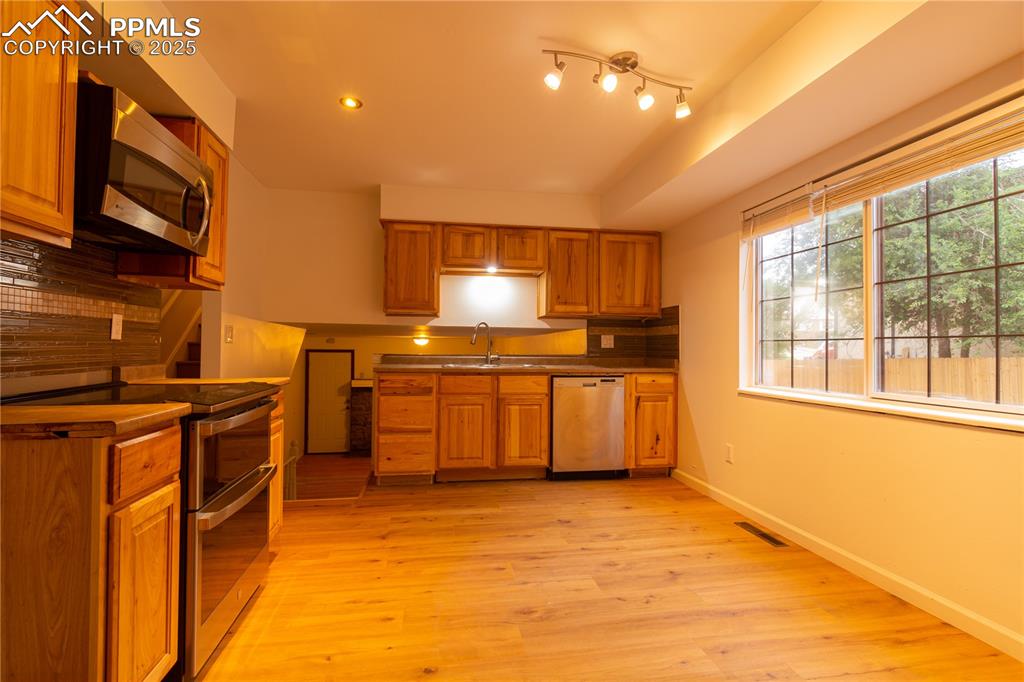 Image 10 of 47: Kitchen with stainless steel appliances, brown cabinets, backsplash, and re