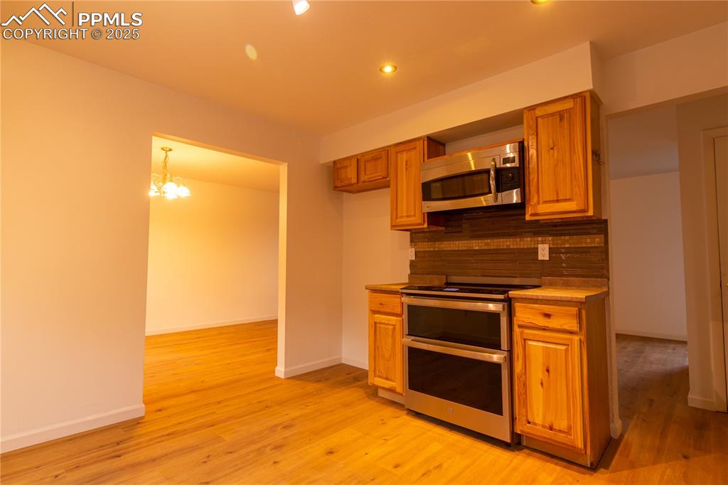 Image 12 of 47: Kitchen featuring stainless steel appliances, decorative backsplash, brown 
