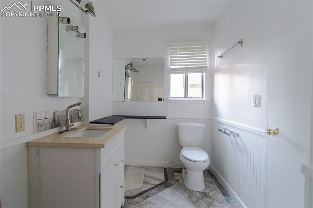 Image 36 of 47: Bathroom with marble look tile flooring, vanity, and a wainscoted wall