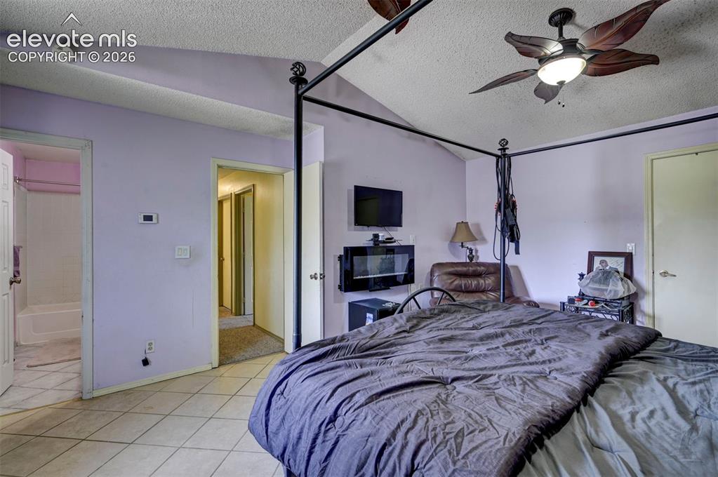 Image 25 of 43: Vaulted ceiling bedroom featuring tile flooring, a wall-mounted electric fi
