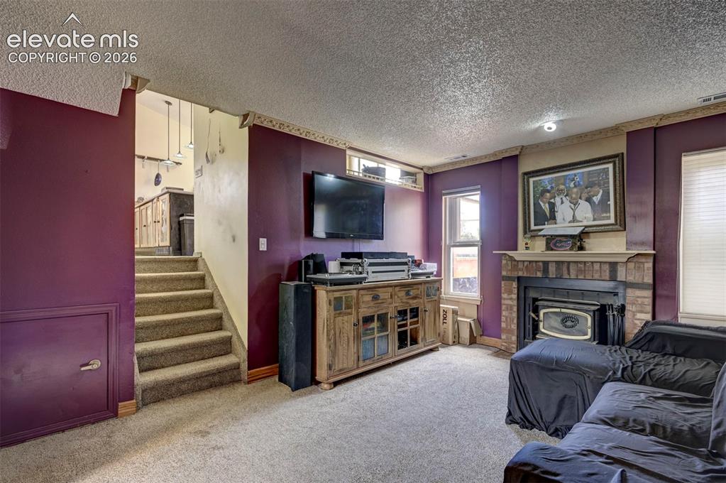 Image 29 of 43: Carpeted living area featuring a brick-surround fireplace with a wood mantl