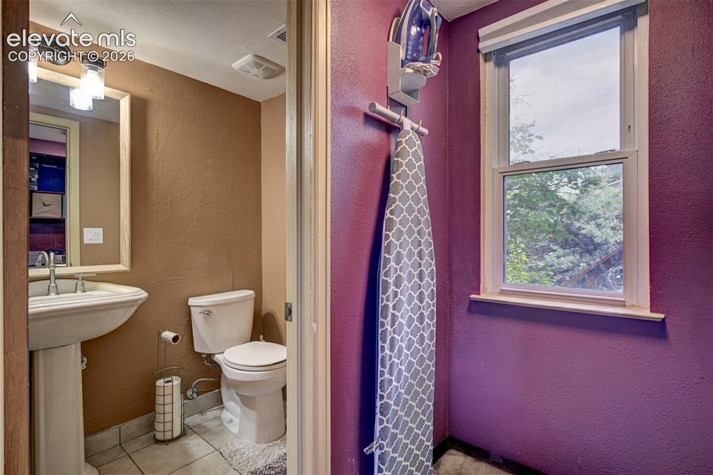 Image 32 of 43: Pedestal sink with chrome faucet, wall-mounted mirror, and overhead lightin