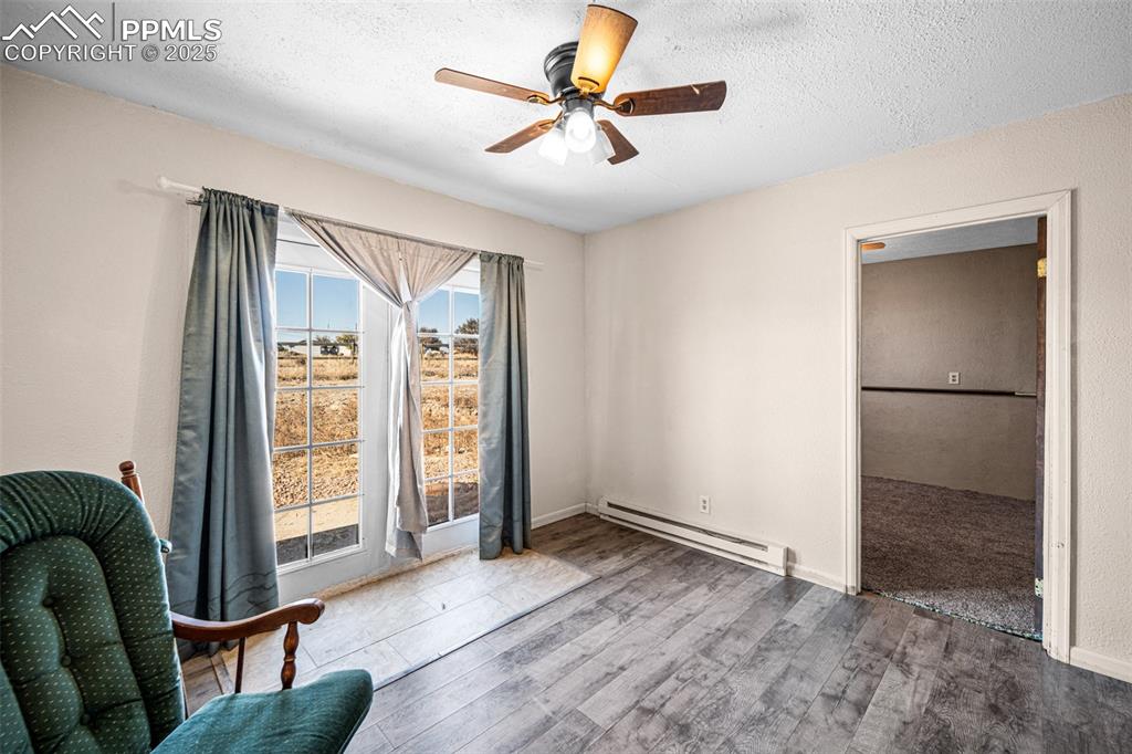 Image 9 of 12: Living area featuring baseboard heating, wood finished floors, a textured c