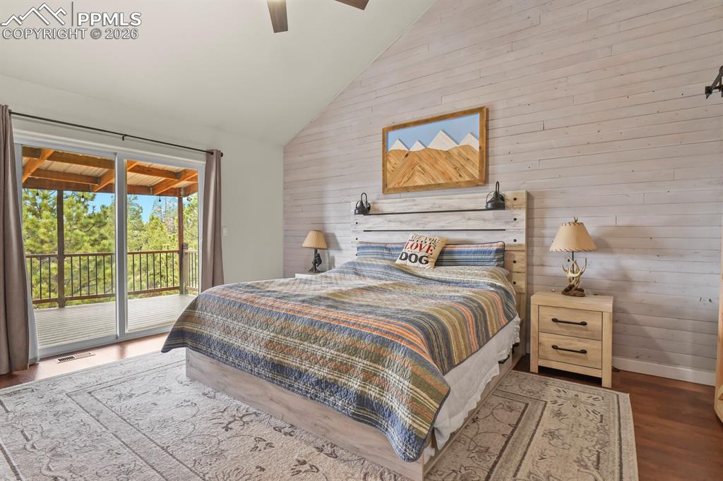 Image 16 of 41: Bedroom with wooden walls, dark wood finished floors, vaulted ceiling, acce