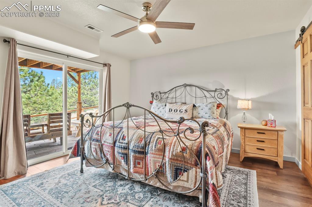 Image 25 of 41: Bedroom with a barn door, access to exterior, a ceiling fan, and wood finis