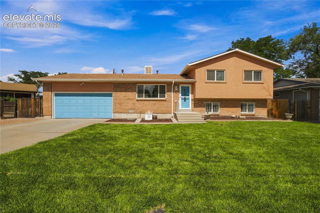 Caption: Brick and stucco exterior with a bright blue garage door, concrete driveway, and a front lawn