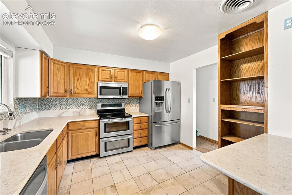 Image 10 of 39: Ceramic tile flooring, light-toned countertops, wood cabinetry, stainless s