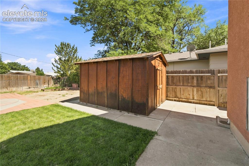 Image 27 of 39: Wood-sided shed, concrete patio, grass lawn, wood fencing, and mature trees
