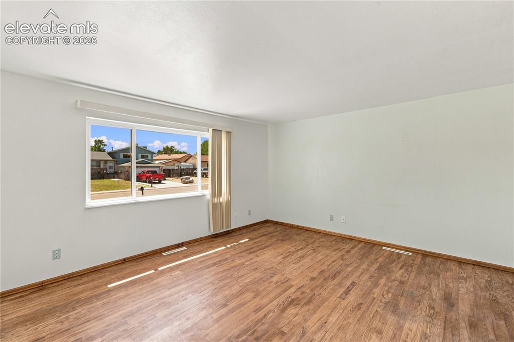 Image 3 of 39: Spacious room featuring wood-finish flooring, white walls, and a large wind