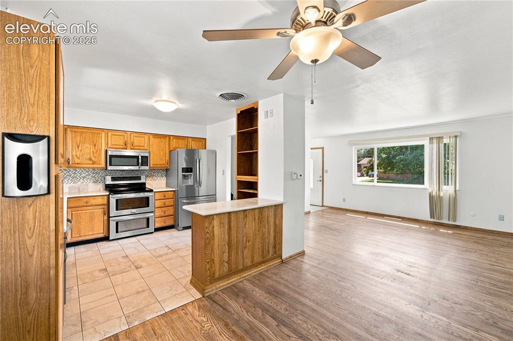 Image 8 of 39: Kitchen with wood cabinetry, stainless steel appliances, and tile backsplas