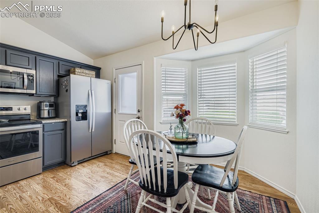 Image 14 of 28: Dining room with light wood-type flooring, vaulted ceiling, and a chandelie
