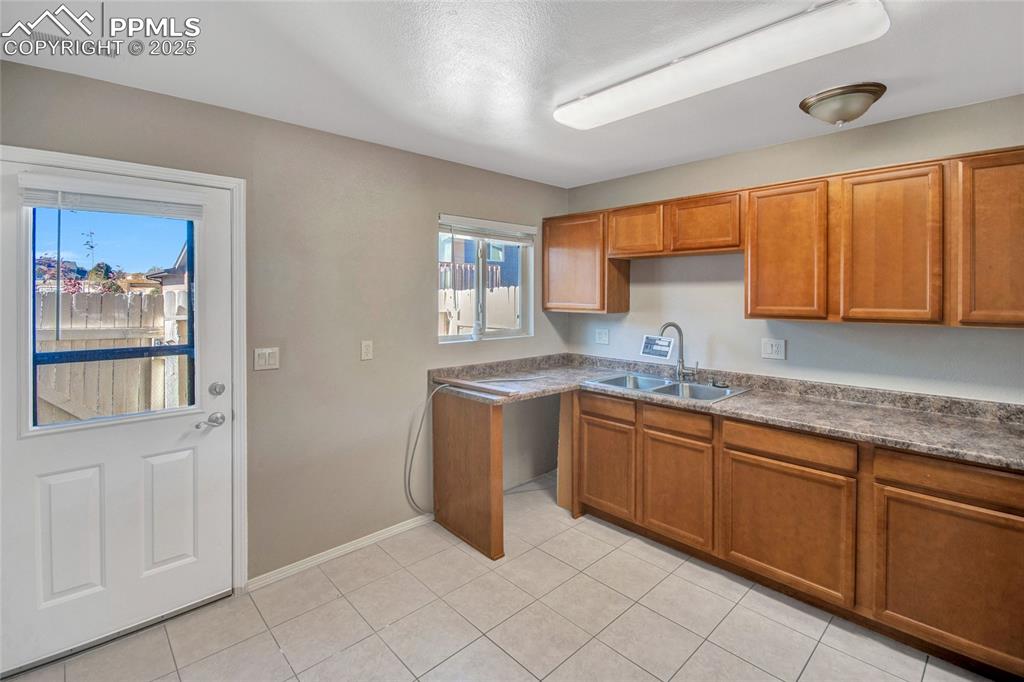 Image 18 of 35: Kitchen with brown cabinetry, light tile patterned floors, and dark counter