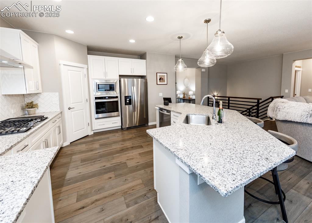 Image 12 of 37: Kitchen with island, white cabinets, wood-style floors, and decorative back