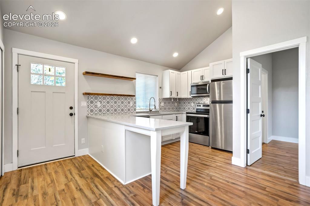Image 30 of 50: Open-concept kitchen featuring wood-finish flooring, white cabinetry, stain