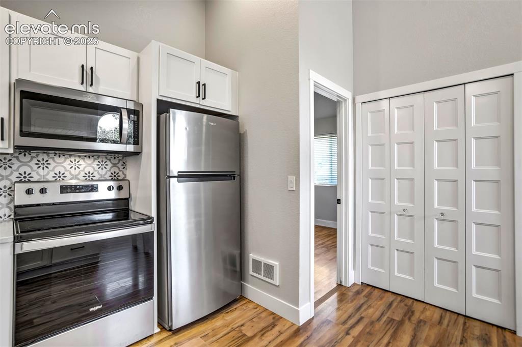 Image 35 of 50: Kitchenette featuring stainless steel appliances, white cabinetry with blac