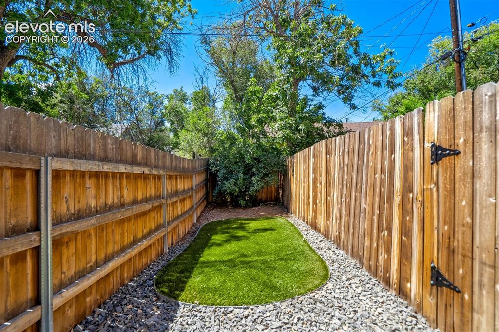 Image 44 of 50: Private backyard area featuring artificial turf, gravel landscaping, and ta