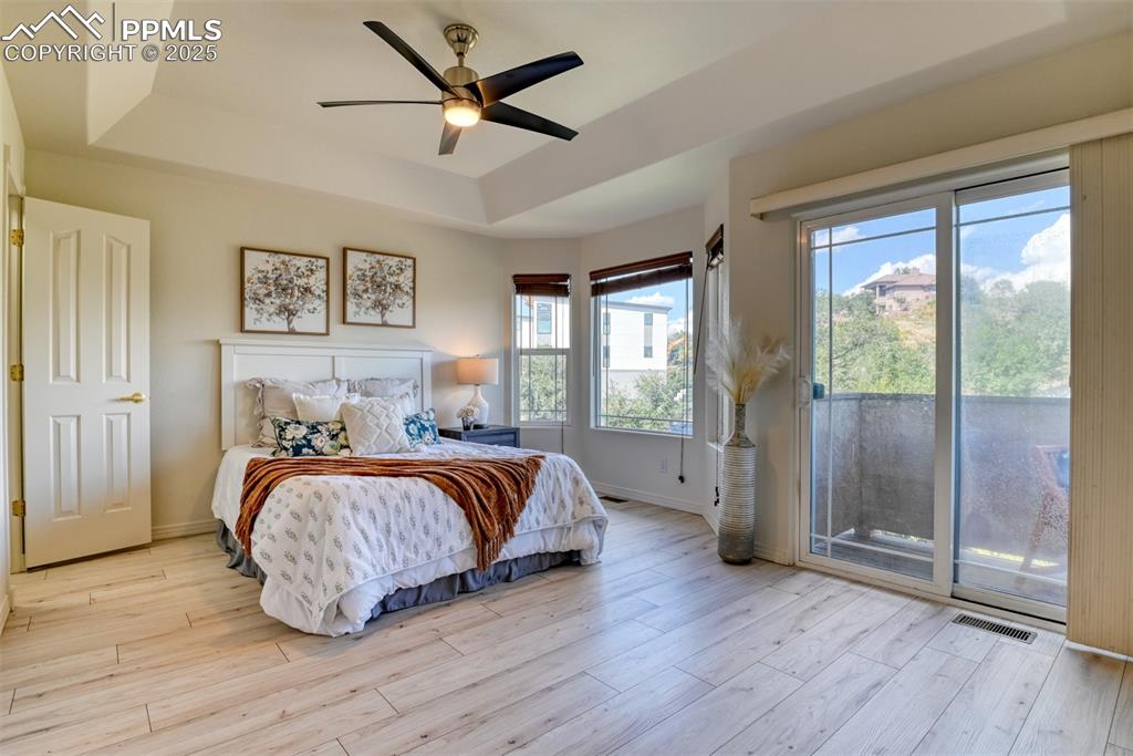 Image 15 of 46: Bedroom featuring a tray ceiling, light wood-type flooring, access to outsi