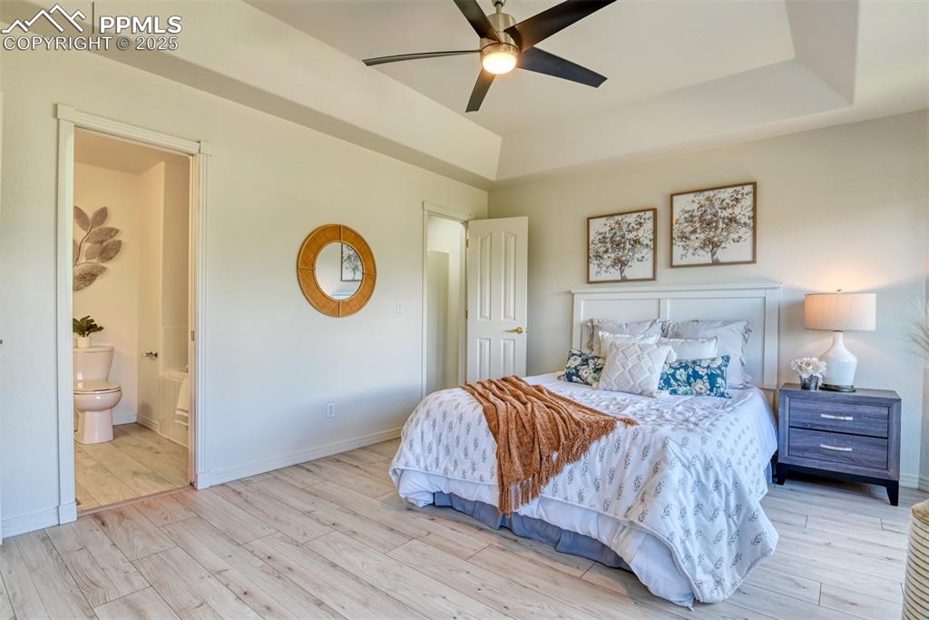 Image 16 of 46: Bedroom with a raised ceiling, wood finished floors, ceiling fan, and conne