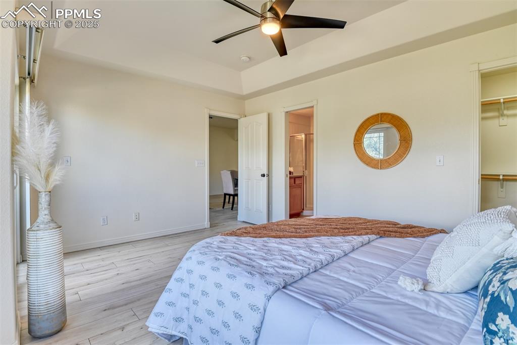 Image 17 of 46: Bedroom with a tray ceiling, wood finished floors, a ceiling fan, connected