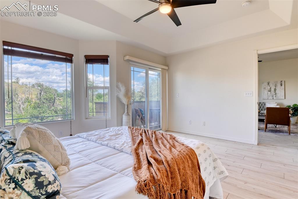 Image 18 of 46: Bedroom with light wood finished floors, a tray ceiling, access to outside,