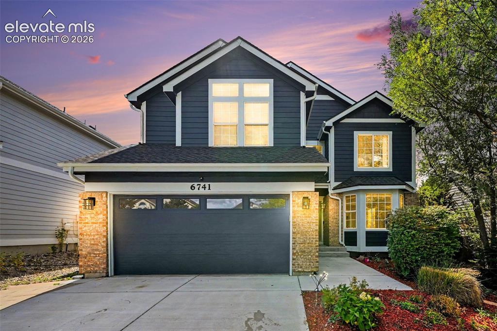 Caption: Blue horizontal siding exterior with stone accents, a dual-pane garage door, bay windows, and a conc