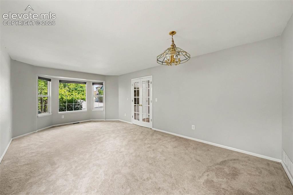 Image 13 of 31: Carpeted room with a bay window, a brass-toned chandelier, and French doors