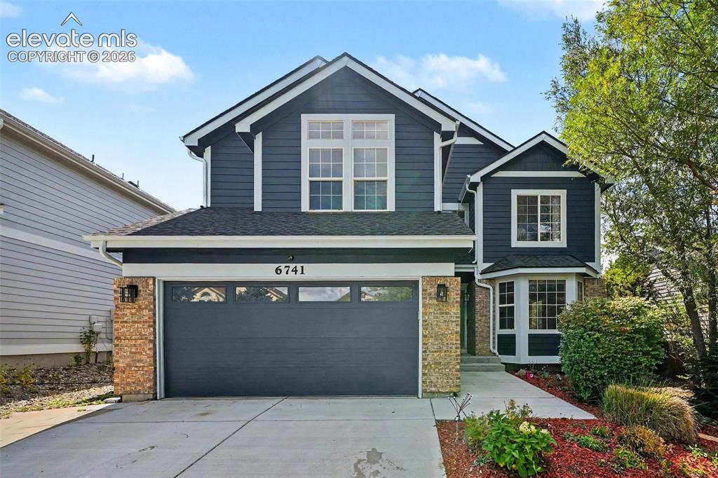 Image 2 of 31: Two-story residence featuring dark siding, stone veneer accents, an attache