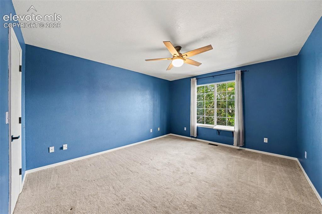 Image 22 of 31: Spacious room with plush carpeting, a large window, and a ceiling fan