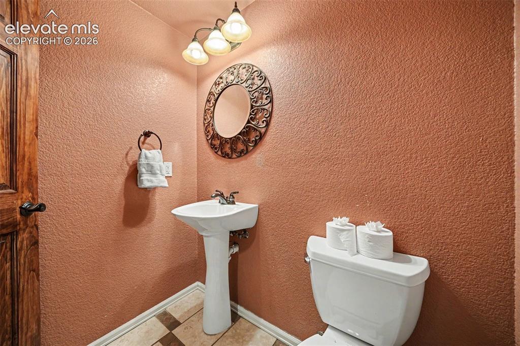 Image 28 of 31: Pedestal sink with chrome fixtures, decorative wall mirror, and three-light