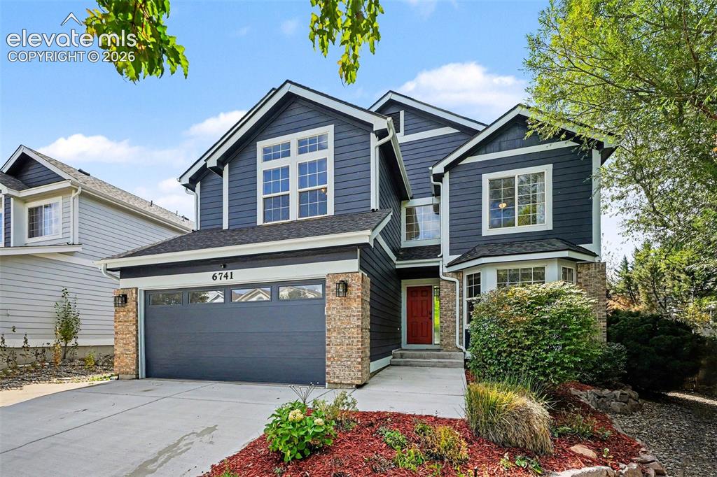 Image 3 of 31: Two-story residence featuring dark blue siding and stone accents