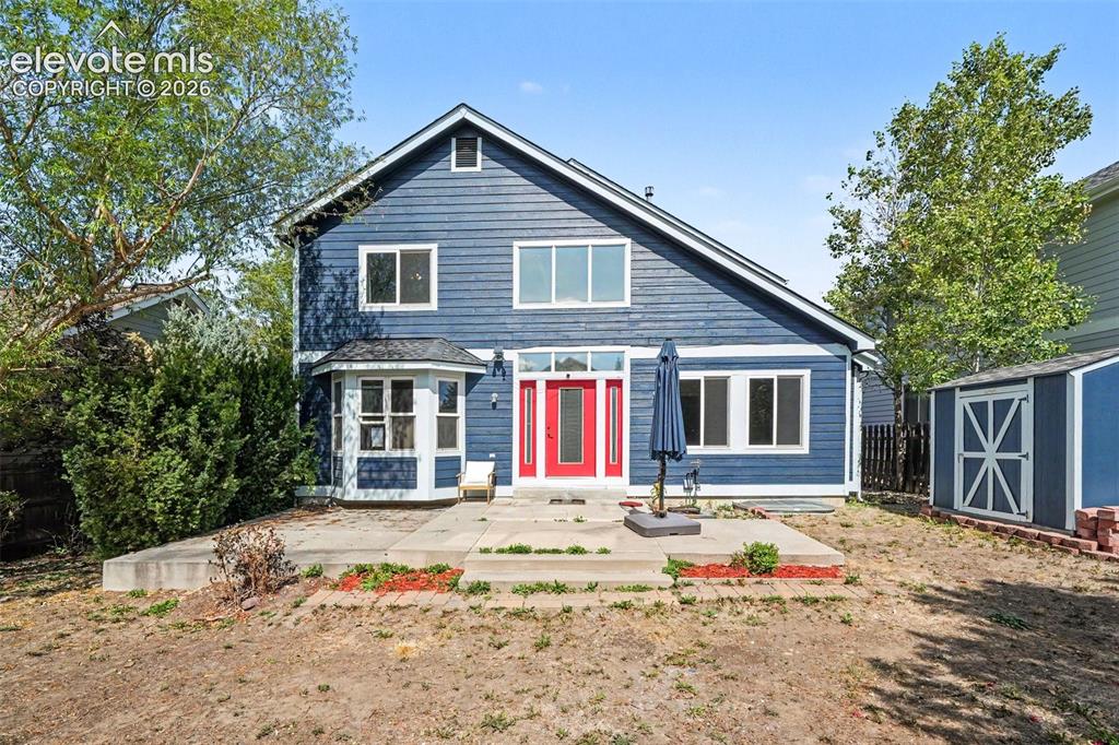 Image 30 of 31: Blue siding exterior with a prominent red entry door, a bay window on the l