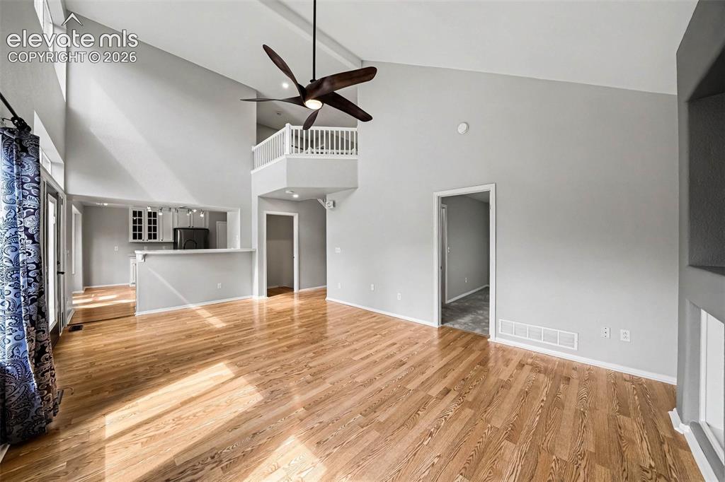 Image 8 of 31: Vaulted ceiling with exposed beams, hardwood flooring, ceiling fan, and an 