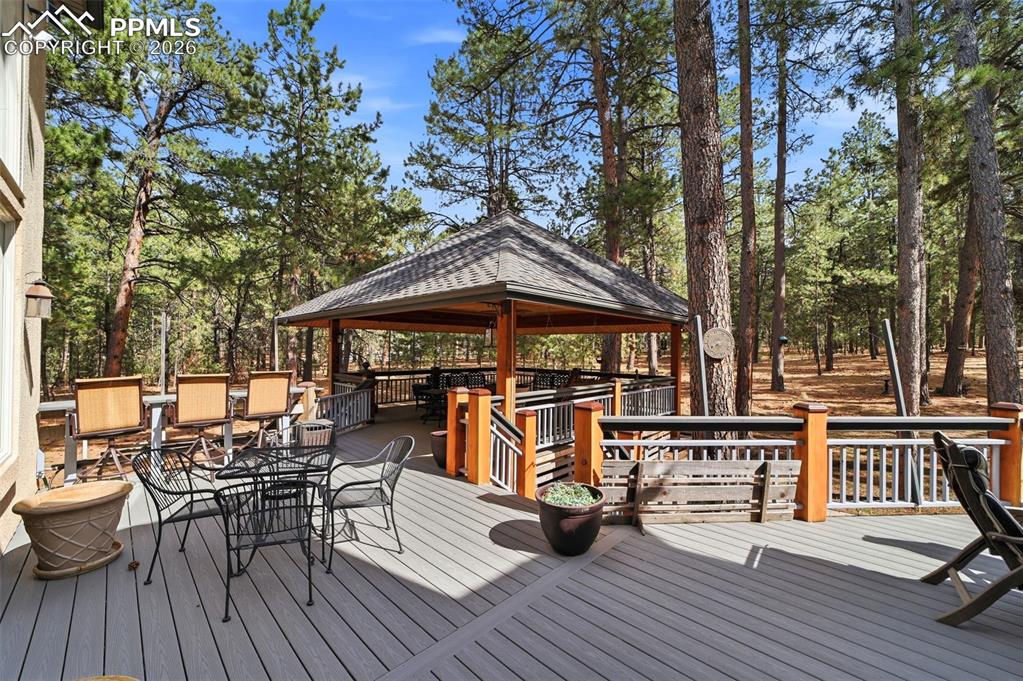 Image 9 of 50: Outdoor terrace with outdoor dining area, a gazebo, and view of wooded area