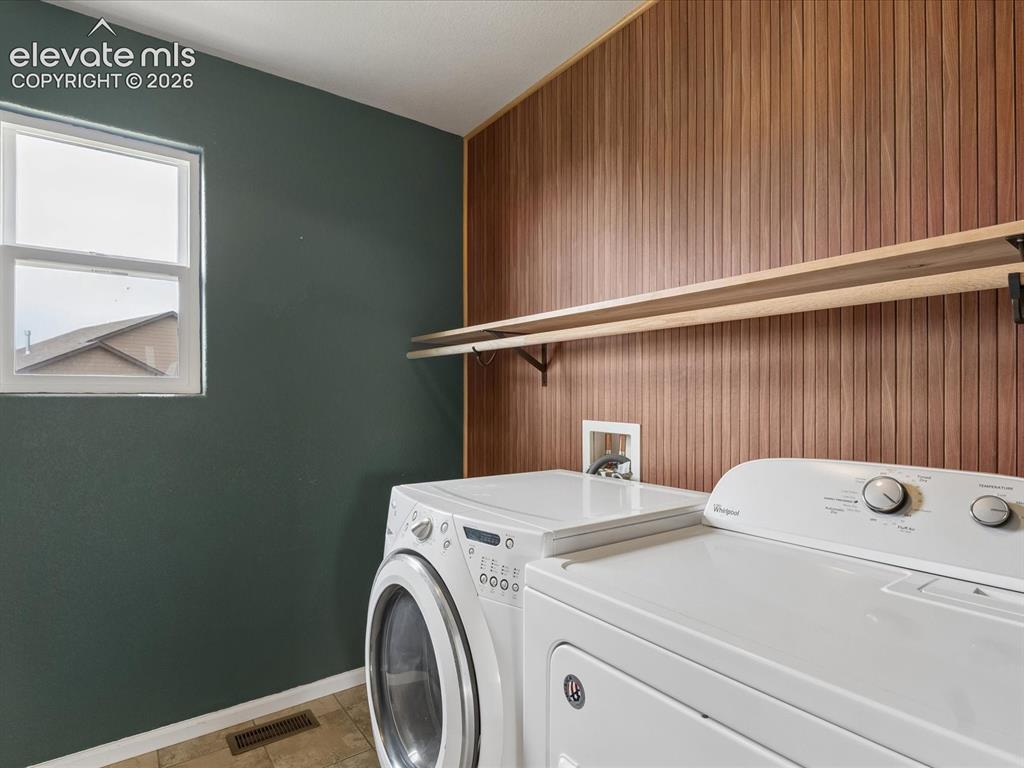 Image 11 of 23: Laundry area featuring a window, wood-paneled accent wall, and built-in she