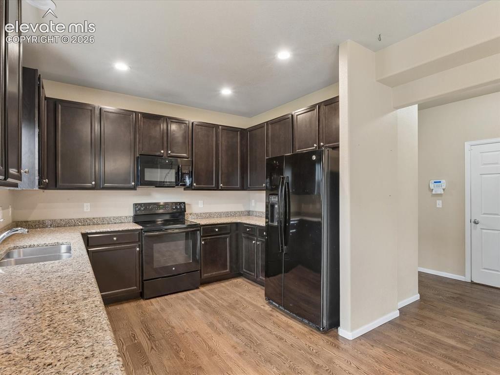 Image 4 of 23: Kitchen featuring dark wood-finish cabinetry, black appliances, speckled co