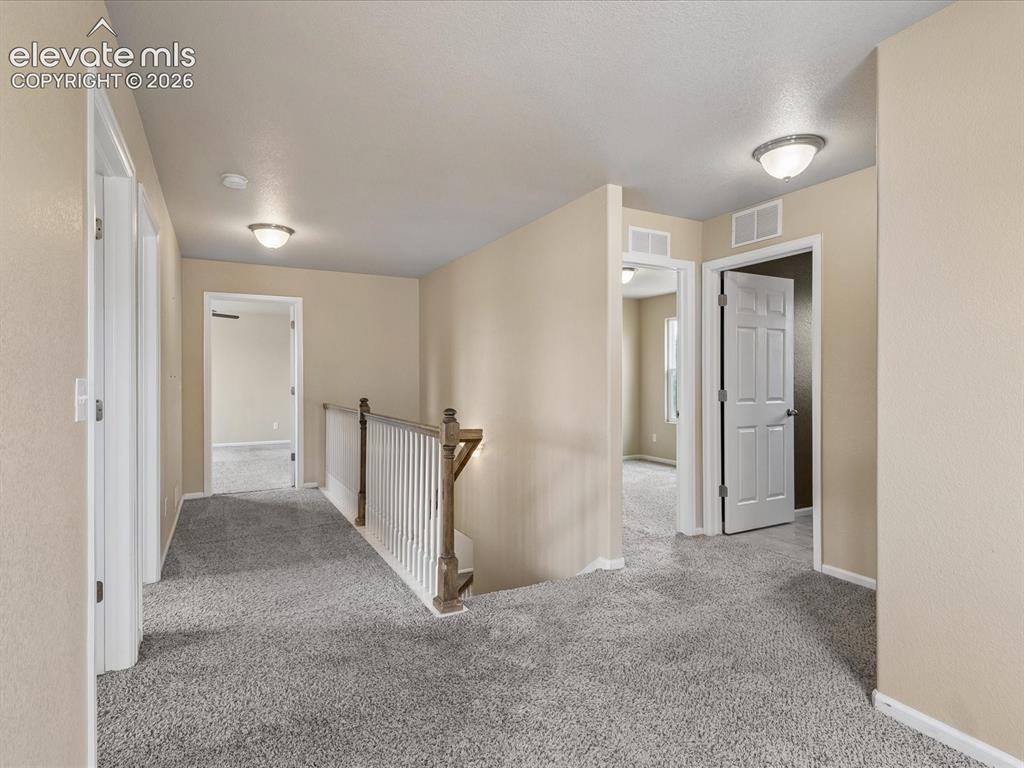 Image 9 of 23: Carpeted hallway featuring a wood-finish and white baluster railing, neutra