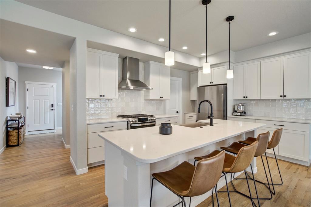 Image 7 of 43: Kitchen featuring wall chimney range hood, a breakfast bar, white cabinets,