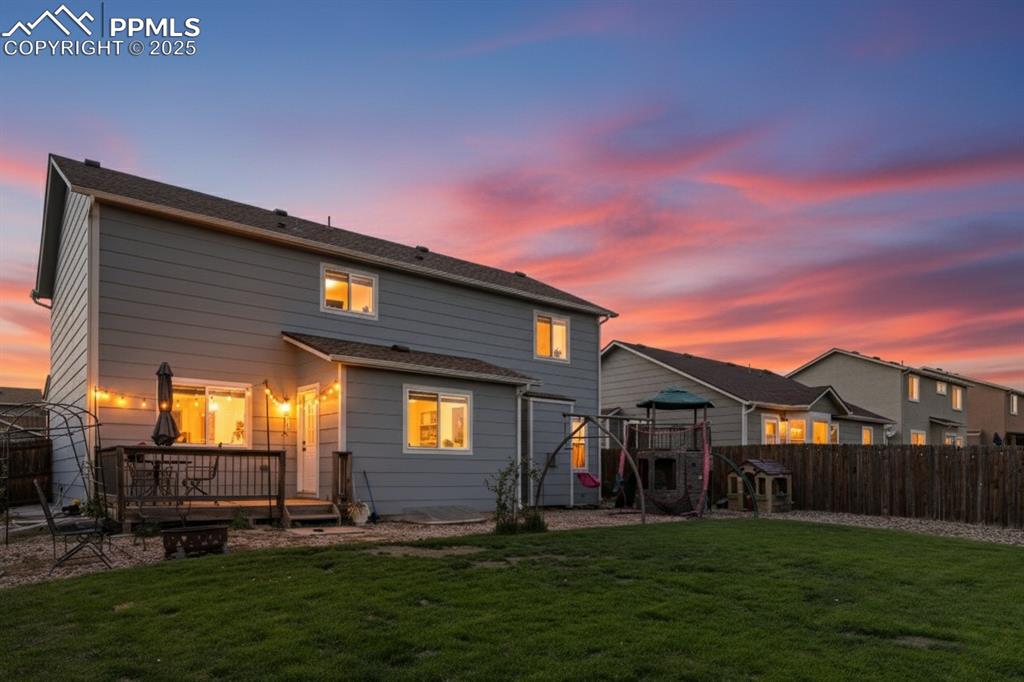 Image 4 of 41: Back of house at dusk with a wooden deck, a playground, and a fenced backya
