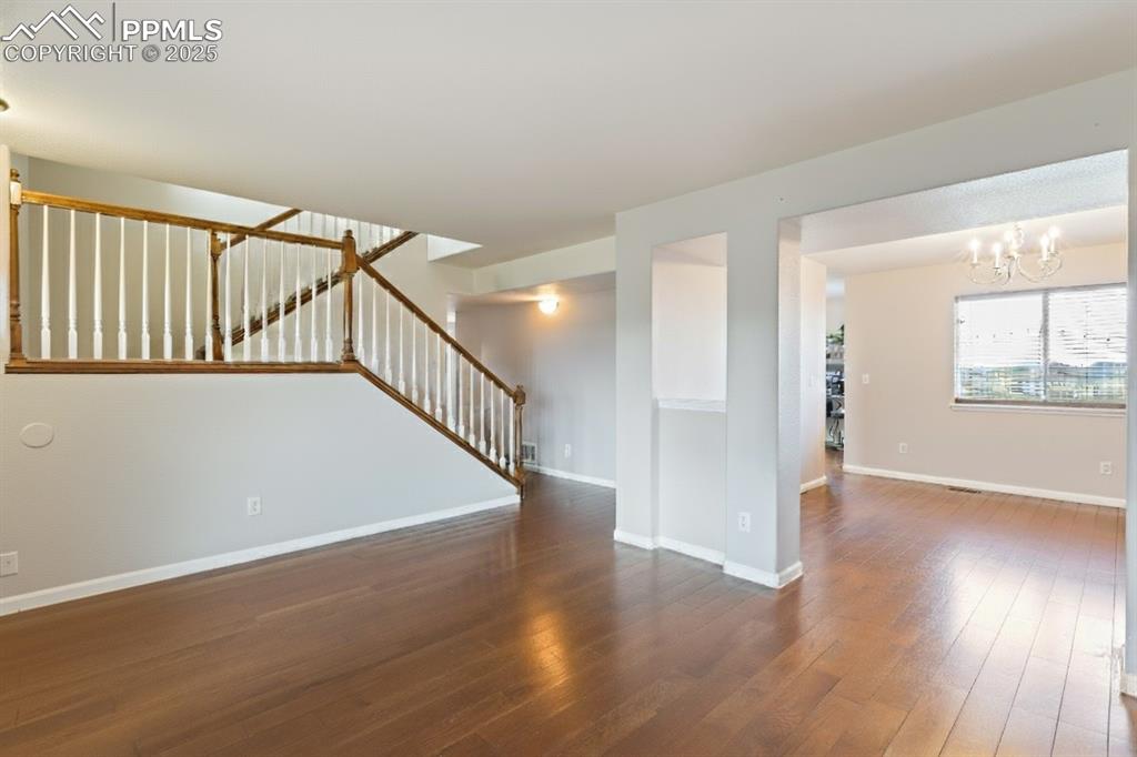 Image 8 of 41: Unfurnished living room with stairs, a chandelier, and dark wood finished f