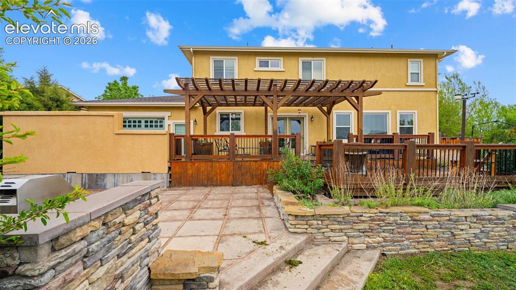 Image 34 of 45: Multi-level backyard featuring a spacious wood deck with pergola, stone ret