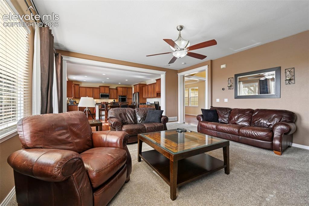 Image 6 of 37: Living area with neutral carpeting, an overhead ceiling fan, and a wide cas