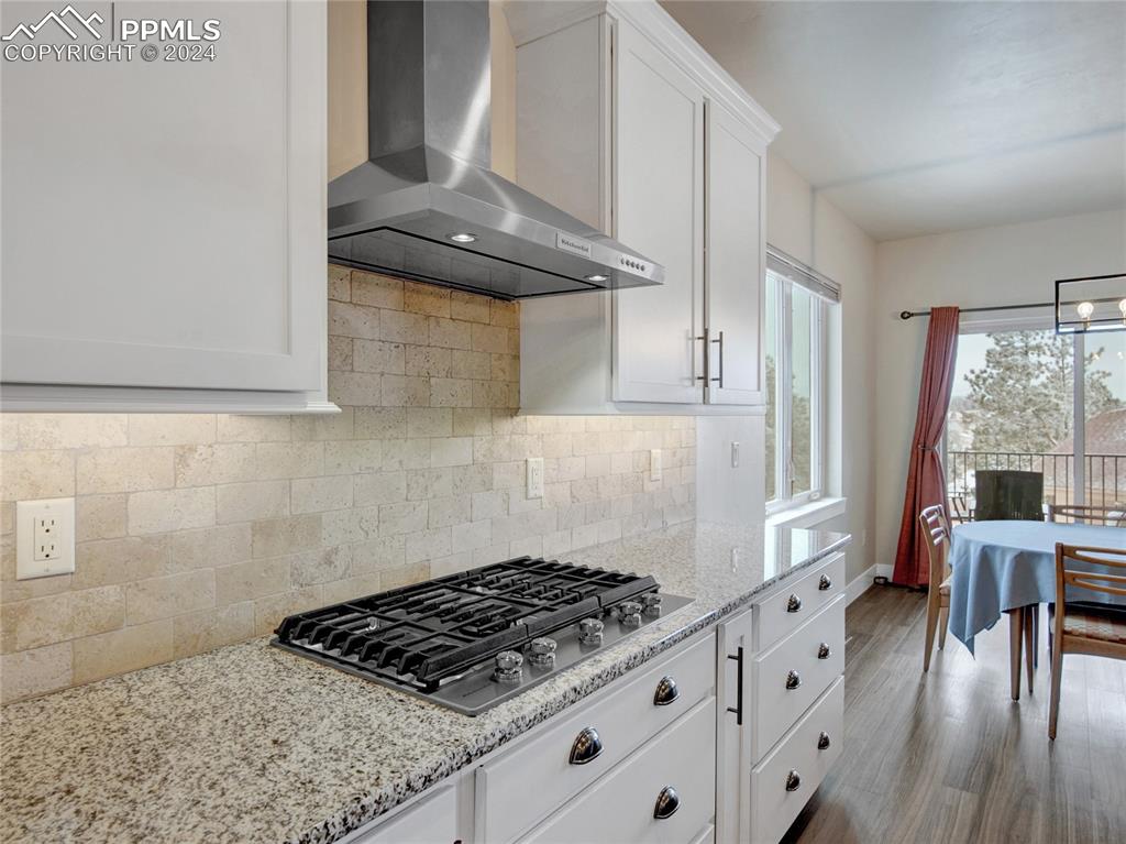 Image 12 of 47: Kitchen with tasteful backsplash, wall chimney exhaust hood, light stone co
