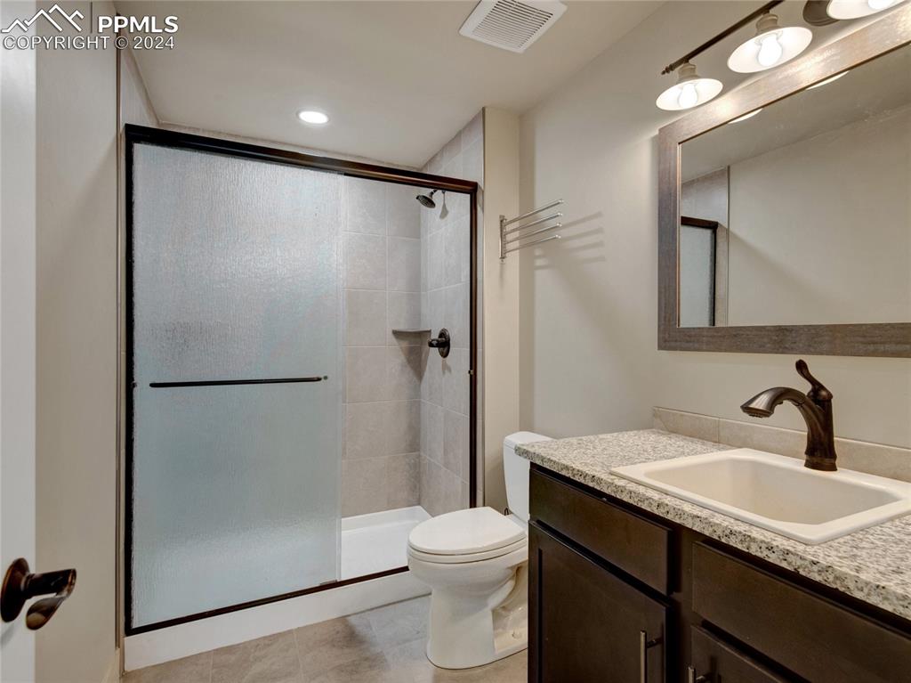 Image 36 of 47: Bathroom with toilet, tile flooring, large vanity, and a shower with door