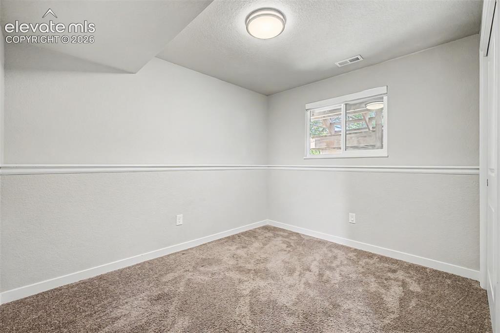 Image 24 of 44: Carpeted 3rd bedroom on the lower level features ample light, neutral walls