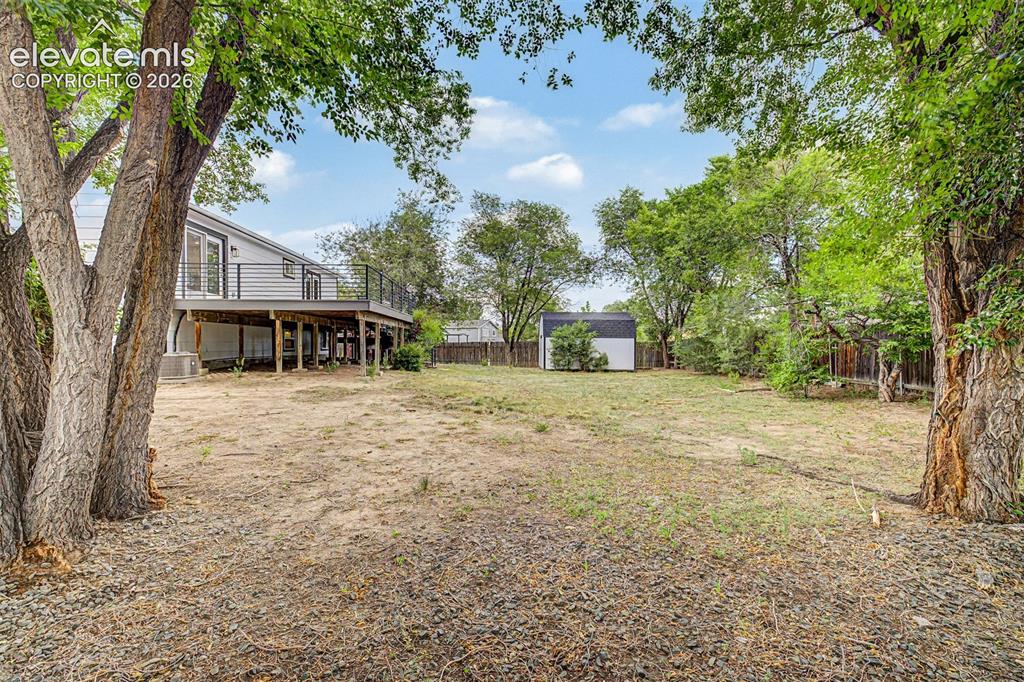 Image 33 of 44: Expansive backyard with mature trees, a detached storage shed, and a raised